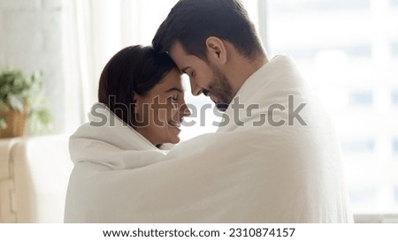 Happy loving couple wrapped in warm blanket touching foreheads with closed eyes and hugging, standing in kitchen at home, smiling beautiful wife and handsome husband enjoying tender moment Royalty-Free Stock Photo #2310874157