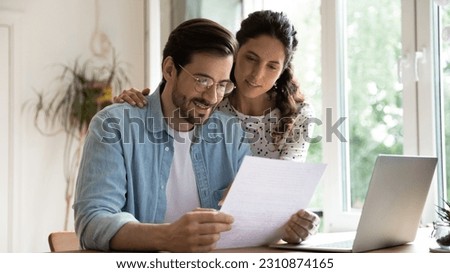 Happy affectionate young family couple reading paper correspondence with good news, feeling curious of getting interested information. Smiling bonding man and woman getting bank notification letter. Royalty-Free Stock Photo #2310874165