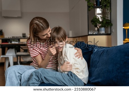 Smiling mother amuses offended little boy. Mom hugs son pokes finger in nose. Reconciliation of parent and children after quarrel. Difficulties of adolescence. Offended schoolboy sit with mom on couch Royalty-Free Stock Photo #2310880067