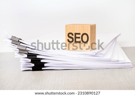 a wooden block with a text SEO on a stack of documents. grey table, white background