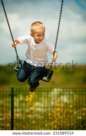 Little blonde boy having fun at the playground. Child kid playing on a swing outdoor. Happy active childhood. Royalty-Free Stock Photo #231089554