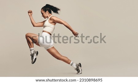 Sports woman jumping forward, running in a studio workout. Wearing sportswear, she combines strength training with cardio exercises to improve fitness. Female athlete pushing herself to new limits. Royalty-Free Stock Photo #2310898695