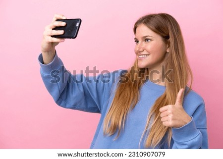 Young blonde woman isolated on pink background making a selfie with mobile phone