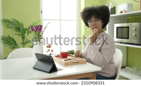 Young african american woman having breakfast watching video on touchpad at home