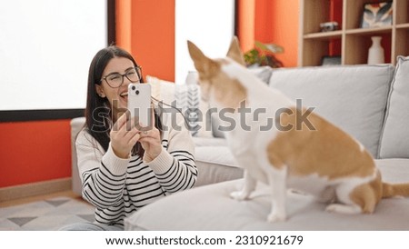 Young hispanic woman with chihuahua dog sitting on the floor taking photo with smartphone at home