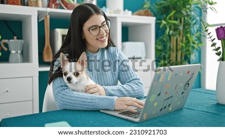 Young hispanic woman with chihuahua dog using laptop at dinning room