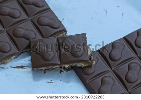 a broken bar of milky delicious brown calorie chocolate with nuts and caramel lies on a white surface