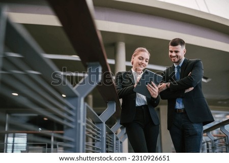Happy businessman showing content on tablet to female colleague. Business man and woman walking outside using tablet and talking, smiling, laughing. Communication concept. Royalty-Free Stock Photo #2310926651