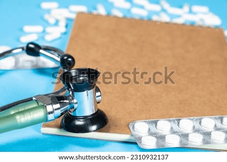 A medical notebook with a stethoscope and pills, a place for text, blue background