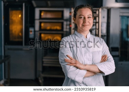 smiling beautiful woman baker in uniform stands near the oven before the start work bakery production of pastries Royalty-Free Stock Photo #2310935819