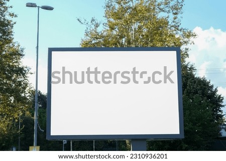 Blank advertising sign board display billboard mockup outside with trees and blue cloudy sky background. White billboard banner background in city. Selective focus of billboard.