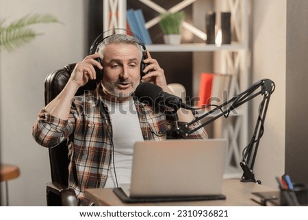 Confident man is putting headphones during online stream. Blogger is doing podcast with professional microphone