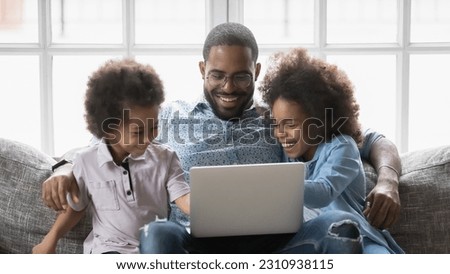 Overjoyed young african American young father sit relax on sofa with little kids watch video cartoon on laptop, smiling biracial loving dad rest on couch with two children using computer together