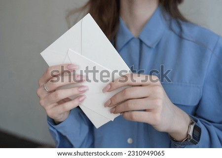 Women's hands hold two milk-colored envelopes. One small, the second large envelope. The concept of invitation to the wedding, bachelorette party, birthday. Mock up with empty space