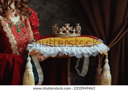 Closeup on medieval queen in red dress with crown on pillow on dark gray background. Royalty-Free Stock Photo #2310949463