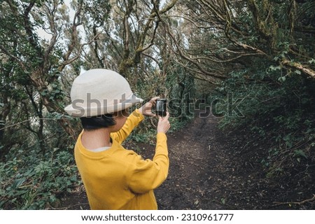 Teenage girl in yellow shirt and straw hat taking pictures of the Anaga forest in Tenerife