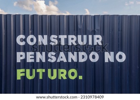 Construction site with the message written in Portuguese: "Build thinking about the future". Metal partition wall in blue color, construction site fence.