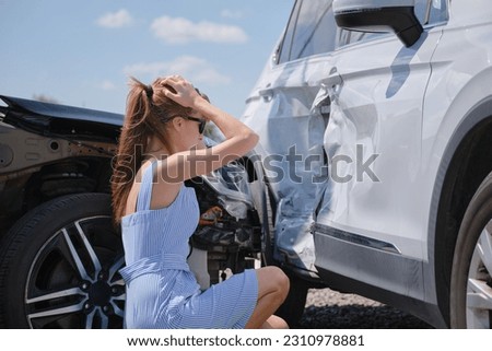 Sad young woman driver sitting near her smashed car looking shocked on crashed vehicles in road accident Royalty-Free Stock Photo #2310978881