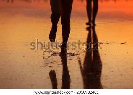 Summer travel holiday. Cropped photo of silhouette legs mom and child daughter walk together on sunset beach. Reflection on water. Mothers day. Concept of family values. International Children's Day.