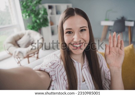 Photo of charming friendly young lady dressed striped shirt recording vlog waving arm palm indoors house room