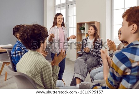 Group of school children friends sitting in a circle in the classroom and listening girl classmate discussing summer holiday applauding her. Junior students talking during a lesson. Royalty-Free Stock Photo #2310995157