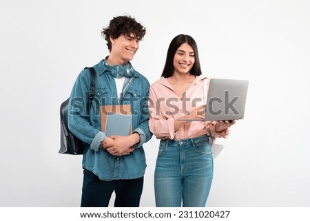 E-Learning. Cheerful Students Couple Using Laptop Computer For Educational Purposes Standing With Backpack And Workbooks Over White Studio Background. Friends Duo Studying Online Together Royalty-Free Stock Photo #2311020427