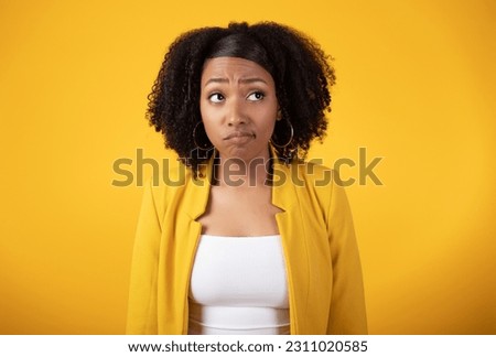 Thoughtful sad young black lady looking aside on yellow studio background, unhappy millennial woman imagining something, feeling doubtful or upset Royalty-Free Stock Photo #2311020585