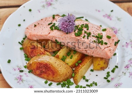 Close up picture of tasty poached or steamed wild salmon fillet served with baked new poptatoes and chopped chives on the rustic porcelain plate. Low calories and healthy dish ideal for balanced diet.