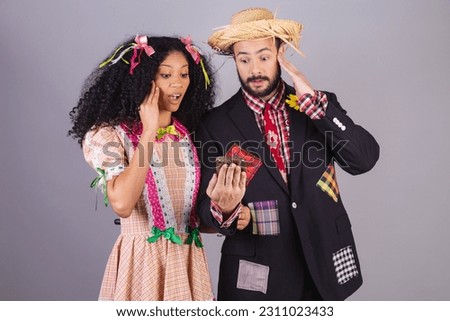 Couple wearing typical clothes of Festa Junina, Arraial, Festa de São João. holding smartphone.