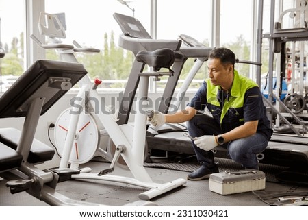 Professional asian male service repair worker or sport fitter using bicycle and treadmill service equipment supervising and securing fitness equipment in indoor gym provide security safety for users. Royalty-Free Stock Photo #2311030421