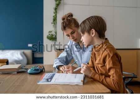 Schoolboy studying with mom, having lesson with private teacher at home, tutor sitting at kitchen table with little boy child explaining exercise, teaching kids foreign language. Homeschooling concept Royalty-Free Stock Photo #2311031681