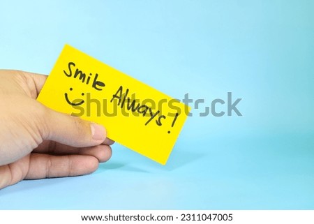 Smile always reminder concept. Hand holding a bright yellow paper message note.	