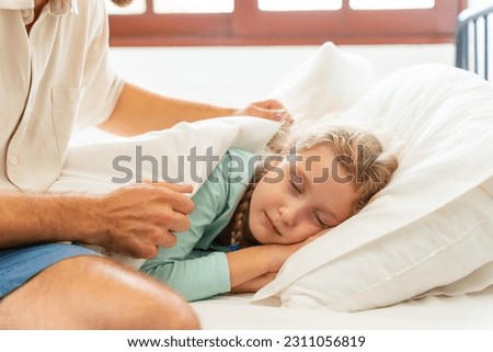 Father wake up a sleeping child daughter on the bed in bedroom in sunny morning. Happy family start a new day together with freshness. Little girl waking up with smiling.