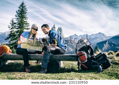 Man and woman hikers hiking in mountains. Young couple camping, looking at map and planning trip or get lost. Getting rest and drinking coffee or tea, navigation and looking for direction