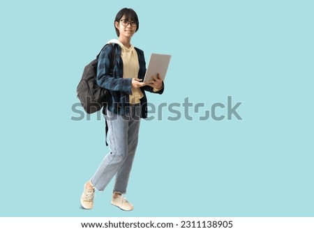 full body portrait Happy Asian teenager girl holding laptop computer and carry backpack, isolated on pastel plain light blue background