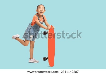 Happy asian smiling little girl holding skateboard, Full body portrait isolated on pastel plain light blue background