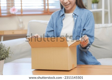Happy excited, asian young woman, girl customer sitting on sofa at home, opening and unpacking cardboard box carton parcel after buying ordering present, shopping online, delivery service concept. Royalty-Free Stock Photo #2311145501