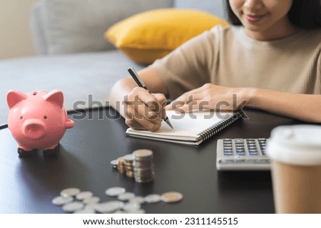 Saving money wealth concept, asian young business woman hand write management budget for saving cost, cash finance planning to spend enough money on her income for save money, payment tax, investing. Royalty-Free Stock Photo #2311145515