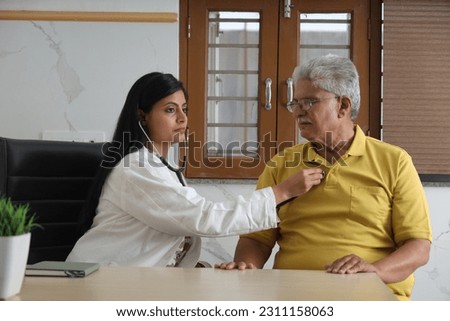 Attractive young Indian doctor sitting with a senior patient. Wide shot of room with doctor consulting an elderly man. An elderly patient getting routine check up by beautiful young doctor.  Royalty-Free Stock Photo #2311158063