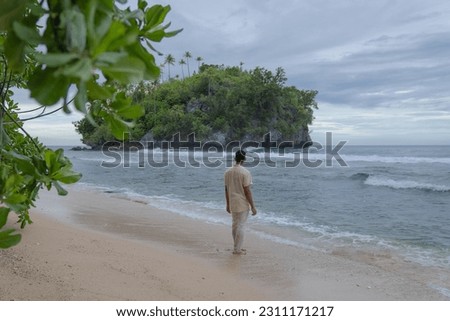 A man walking on a white sandy beach near a beautiful island