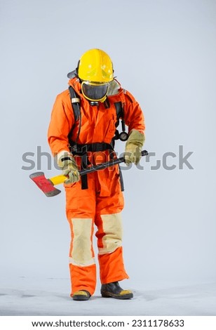 Professional firefighter donning a yellow helmet stands with a resolute presence against a clean white backdrop engrossed in a meticulous examination of the iron axe held firmly in their hands.