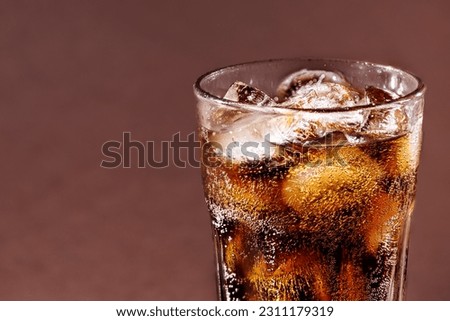 A glass of cola drink with ice cubes. Fresh cold sweet cola drink with ice on brown background with copy space.