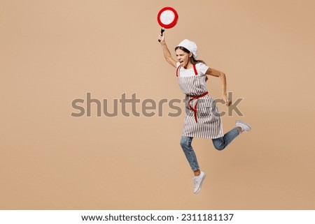 Full body sideways mad sad young housewife housekeeper chef baker latin woman wear apron toque hat run fast threat with frying pan isolated on plain pastel light beige background. Cook food concept Royalty-Free Stock Photo #2311181137