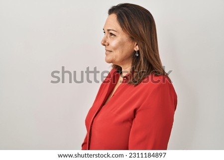 Hispanic mature woman standing over white background looking to side, relax profile pose with natural face with confident smile.  Royalty-Free Stock Photo #2311184897
