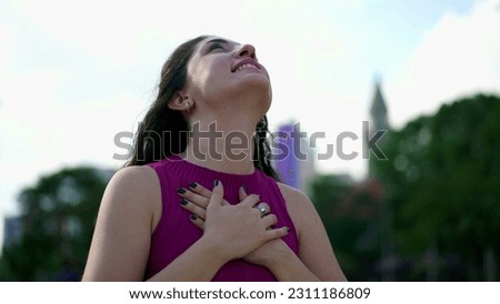 Serene young woman putting hands in chest gazing upwards at sky. Happy person feeling peace and tranquility Royalty-Free Stock Photo #2311186809