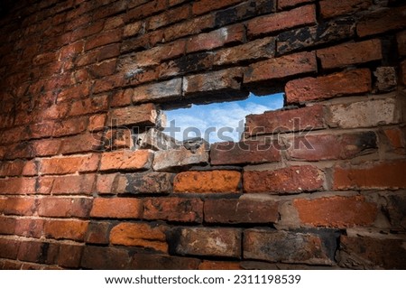 A hole in an old brick wall revealing a blue sky.
