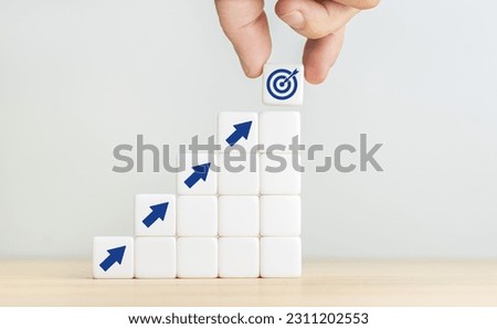 Business goal and objective target concept. Hand holding a cube with dartboard and arrows on stacked blocks. Copy space