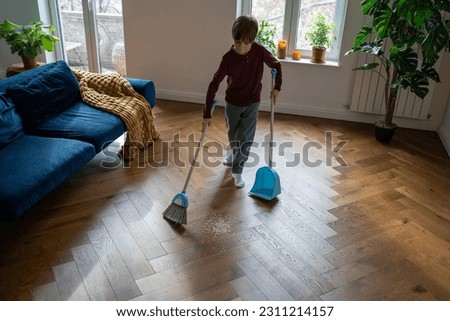 Independent child boy. Habit of cleaning house since childhood. Focused schoolboy sweeps floor from scattered debris with broom with brush and dustpan. Kid do house chores, domestic cleanup. Royalty-Free Stock Photo #2311214157