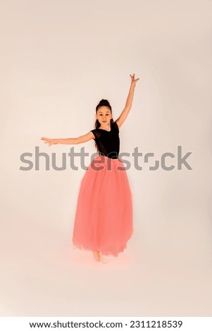 Ballet concept. A girl in a black gymnastic leotard in a beautiful graceful pose on a white background in pointe shoes and a pink skirt. Front view