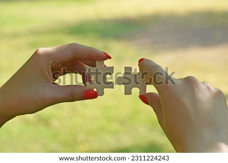 A woman's hands connecting jigsaw puzzle pieces on a natural background - concept of business strategy